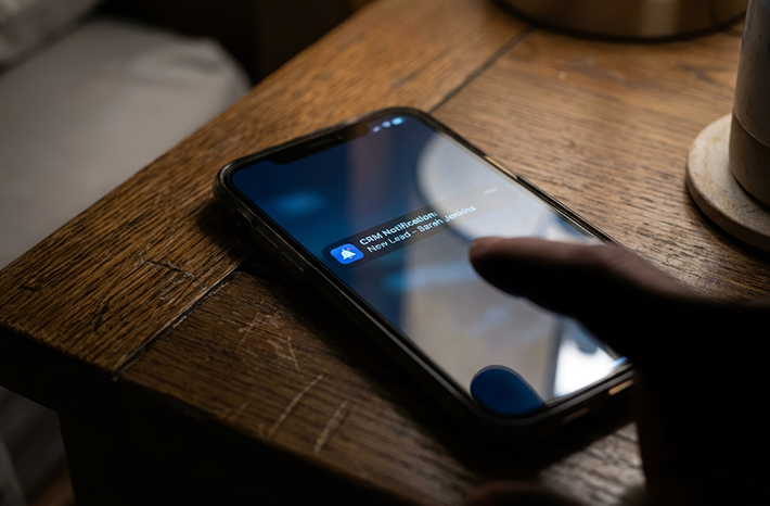 Glowing smartphone on a dark wooden bedside table at night, displaying a new lead notification.